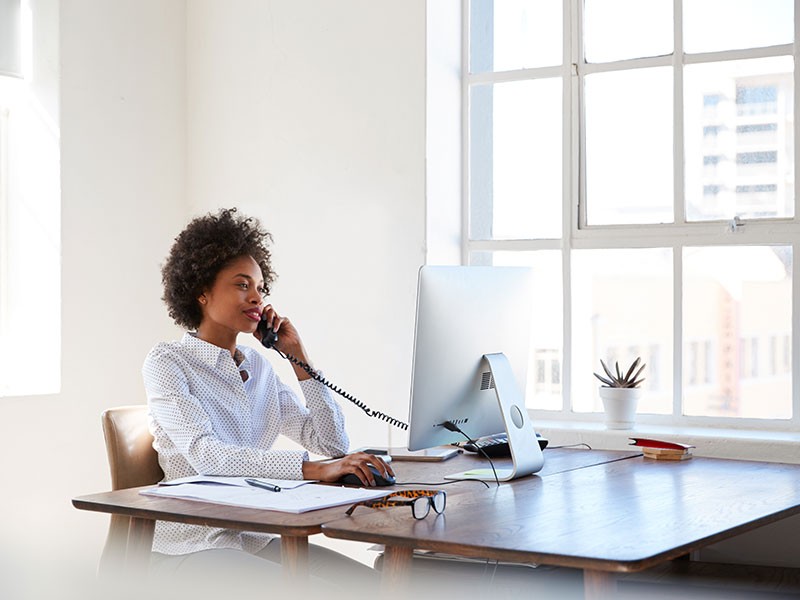 Businesswoman working on computer in office and talking on wired telephone