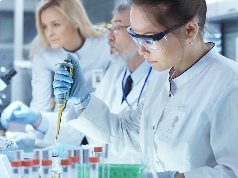 Team of Research Scientists Working With Personal Computer, Analysing Test Trial New Generation Drug Data and Using Micropipette for Filling Test Tubes. They Work in a Modern Laboratory Center