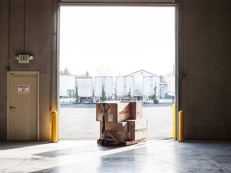 A small stack of products in boxes sitting on a manual pallet jack in a loading dock door at a distribution warehouse.