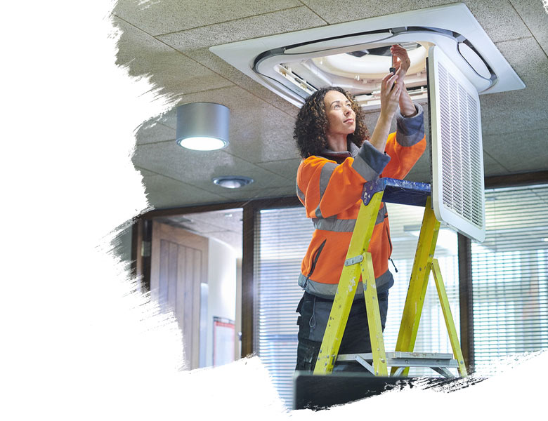 Female facilities maintenance engineer works on ceiling repair in an office on campus